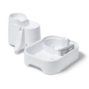 Eine Frontalansicht des weißen dreistufigen Haustierbrunnes, der in zwei Teile getrennt ist und das Innere der unteren Ebene des Brunnens zeigt, welches das Filtergehäuse und die Wasserlinie des Reservoirs umfasst, vor weißem Hintergrund