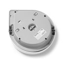 Die Unterseite eines grauen automatischen Haustierfütterers, die dessen Basiskonstruktion zeigt. Das runde Gerät hat einen glatten Kunststoffboden mit vier schwarzen Gummifüßen, die um den Umfang herum positioniert sind, um Stabilität zu gewährleisten. Es gibt eine zentrale kreuzförmige Vertiefung in der Mitte, und mehrere Befestigungspunkte und strukturelle Elemente sind sichtbar. Ein weißes Produktetikett mit Text und behördlichen Kennzeichnungen ist an der Basis befestigt.