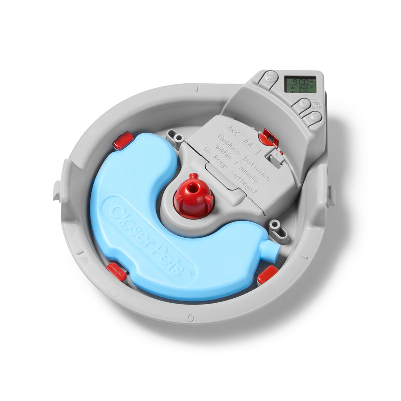 "Eine geöffnete Ansicht eines grauen automatischen Haustierfütterers von Closer Pets, die den internen Mechanismus zeigt. Das runde Gerät hat einen hellblauen Futterbehälter-Einsatz, der sich um das Innere krümmt, mit einem zentralen weißen Rotationsmechanismus mit roten Bedienknöpfen. Es gibt rote Akzentpunkte um den Umfang herum. Ein digitales Anzeigepanel ist in der oberen rechten Ecke sichtbar und zeigt einen grünen LCD-Bildschirm. Der Fütterer scheint ein programmierbares Portionskontrollsystem zu sein